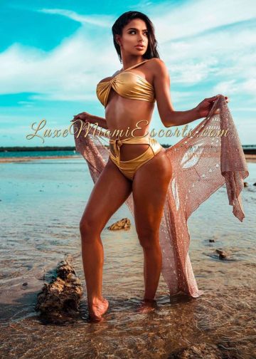 Miranda posing on the beach in golden swimwear