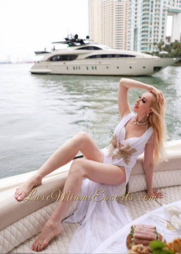 Hot Miami escort model Ruslana posing by the bay, wearing sexy white dress and has a yacht on a background