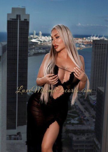 Escort Miami Oksana posing by the window, wearing sexy black outfit