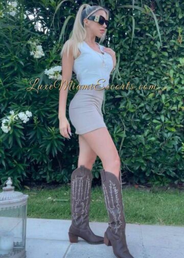 Blonde Miami escort Teresa posing on a street, wearing short skirt, tall boots and white top