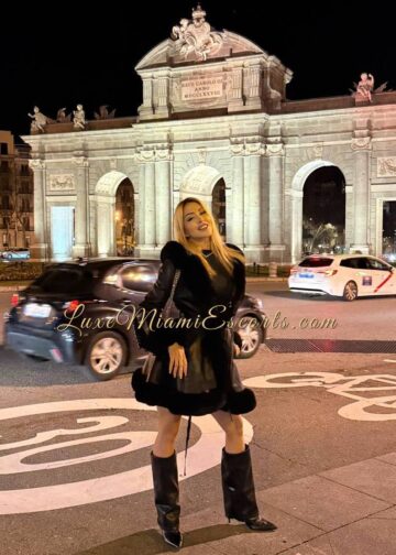 Teresa posing on a street, wearing black winter coat and tall black boots