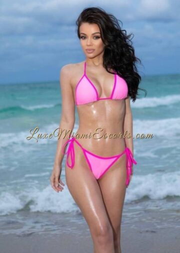 Miami escorts model Lena posing by the ocean in pink swimwear