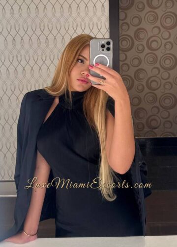 Selfie of escort Miami Kiara, taken in the mirror, wearing black dress and jacket