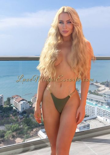 Miami blonde escort Gabriela posing in her green swimwear, covering her breast with her long hair