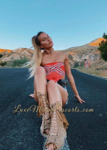 Professional photo of escort Miami - Dina, posing by sitting on the road while wearing denim and red top