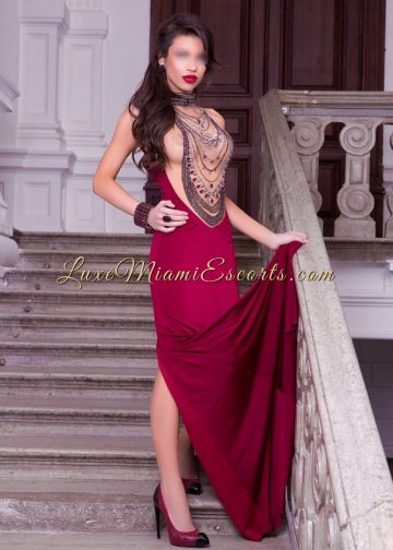 High class Miami escort Camila standing on a stairs in her long burgundy evening dress and black and burgundy high heels